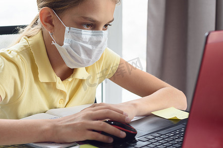 戴着医用口罩的女孩正在电脑前学习。