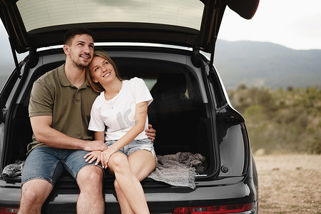 公路摄影照片_年轻快乐的夫妇坐在汽车后备箱里进行公路旅行