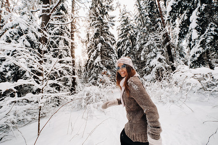冬天，一个穿着毛衣和眼镜的女孩在白雪覆盖的森林里散步