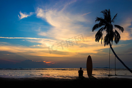 冲浪人的剪影坐在沙滩上的冲浪板上。