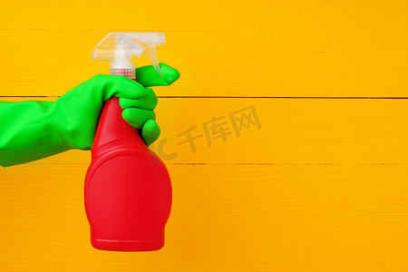 手戴手套，拿着黄色木质背景的家用洗涤剂喷雾