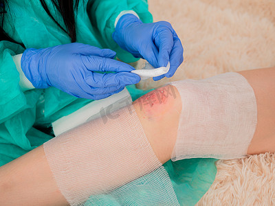 擦伤口摄影照片_一位女医生在她的办公室里给一名十几岁女孩膝盖上的擦伤处包扎绷带。
