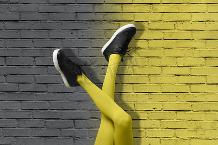 新的黑色女运动鞋，穿着黄色紧身衣的细长女孩腿，背景是渐变黄色和灰色砖墙。 