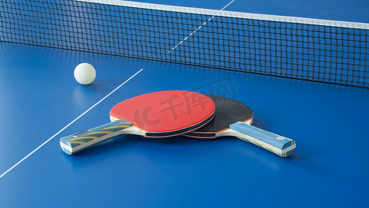 乒乓球运动摄影照片_在蓝色桌上的乒乓球黑色和红色球拍