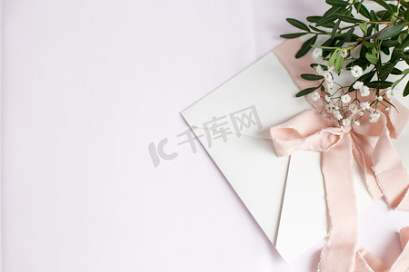 白色粉红色背景的信封，带有桃色丝带和粉红色花朵。