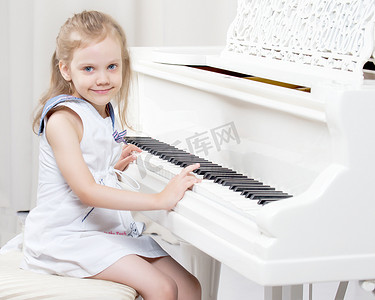 美丽的小女孩正在一架白色的三角钢琴上弹奏。