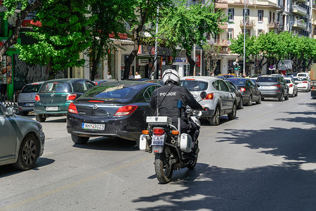 塞萨洛尼基摄影照片_塞萨洛尼基，希腊 Hellenice 警察戴着头盔骑摩托车巡逻。