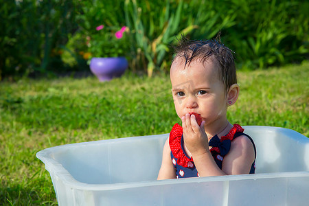 独立浴缸摄影照片_一个小女孩在炎热的天气里穿着泳衣爬进浴缸吃草莓