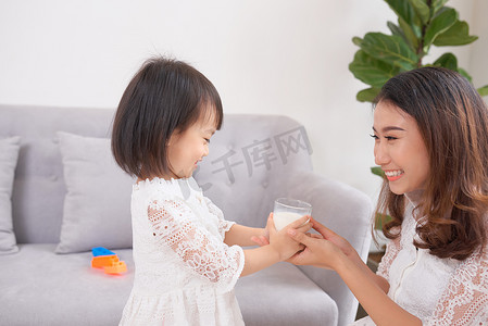 女性喝水摄影照片_小女孩和她妈妈坐在家里的沙发上喝牛奶。