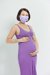 孕妇生病摄影照片_冠状病毒大流行，戴着防护医用口罩的年轻孕妇捂着肚子