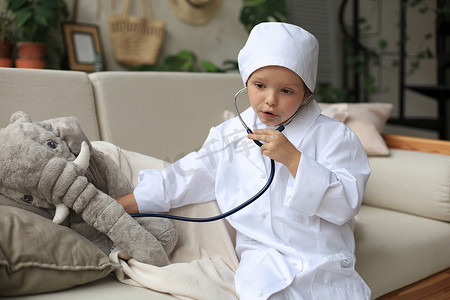 可爱的大象摄影照片_可爱的孩子打扮成医生玩玩具大象，用听诊器检查它的呼吸。
