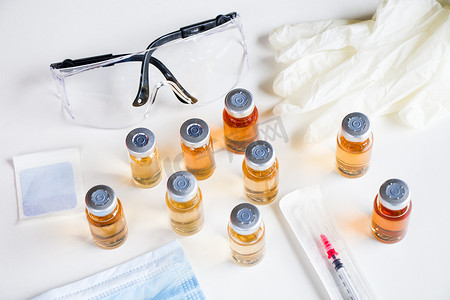 冠摄影照片_安瓿和瓶子、针头、手套和安全玻璃中的新疫苗。
