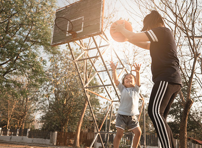 夏日，可爱的亚洲小孩和妈妈在操场上打篮球。