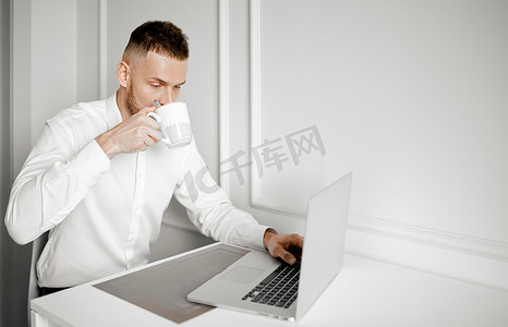 一名男子在厨房里用笔记本电脑工作时喝咖啡