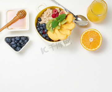 白盘子摄影照片_盘子里放着燕麦片和水果，半个熟橙子和鲜榨果汁放在透明玻璃醒酒器里，蜂蜜放在白桌上的碗里。