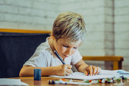 金发可爱的学龄前男孩拿着笔笔记本，表情严肃，努力学习写字，面部表情手势。
