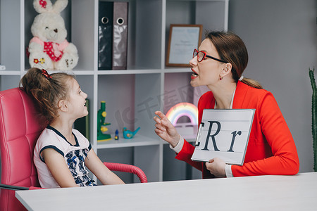 b字母logo摄影照片_言语治疗师教女孩们说字母 R。女性言语语言治疗师教学龄前儿童声音发音。