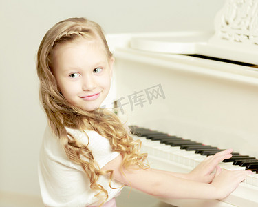 一个小女孩坐在白色钢琴前。