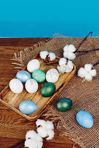 黑板蓝色背景摄影照片_黑板上的复活节彩蛋和粗麻布蓝色背景中的白花