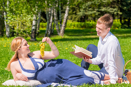 拿着葡萄的孕妇和她的丈夫拿着一本关于照片的书
