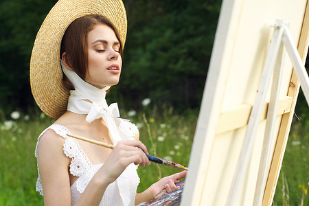 戴帽子的漂亮女人艺术家在自然颜料上画了一幅画