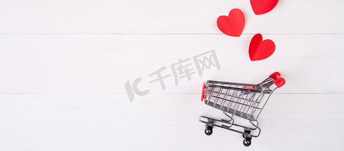 木桌上的购物车和心形纸，2 月 14 日节日情人节的销售概念，超市和商店，符号和庆典，商业和销售的节日概念。