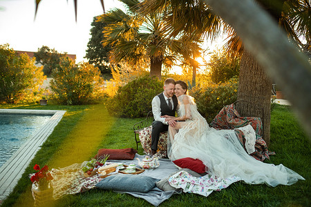 共创幸福家园摄影照片_日落时分，新婚夫妇在草坪上共进晚餐。法国日落时分，一对夫妇坐着喝茶