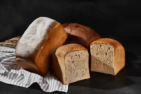 厨房毛巾上放着各种美味的烤面包，整个面包和切成两半的面包，撒上面粉和小麦。