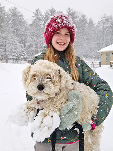 结满了摄影照片_一个微笑的小女孩举起她那只毛茸茸的狗的肖像，狗的爪子上结满了雪