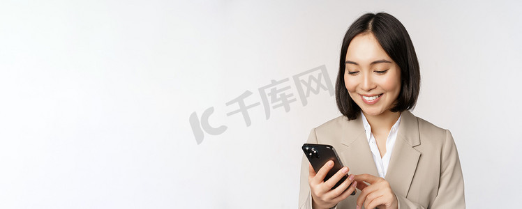 韩国女性、穿西装的企业女士的特写肖像，用手机微笑，拿着智能手机，站在白色背景上