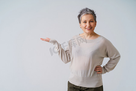灰白的头发摄影照片_美丽、华丽的 50 年代成熟女性，头发灰白，举起手来为您的产品植入隔离在白色背景。
