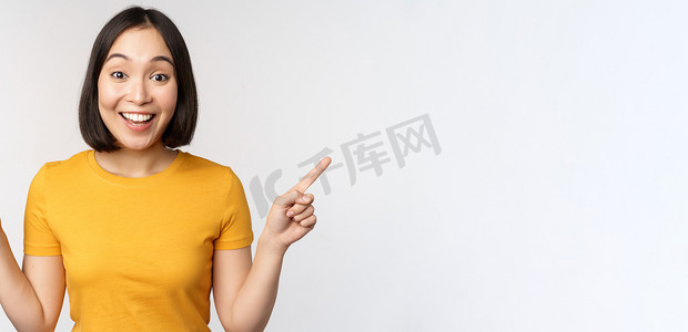 手指左右摄影照片_可爱的亚洲女孩侧指手指，展示左右促销，两种选择，产品变体，站在白色背景的黄色 T 恤上