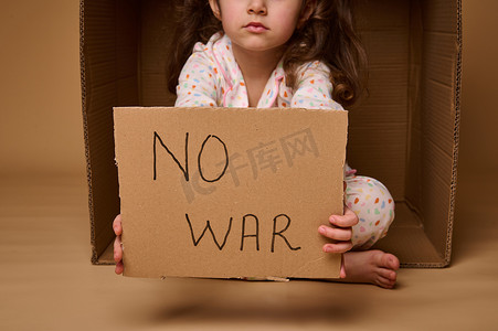 停止战争摄影照片_在该国政治和军事冲突期间，欧洲儿童小女孩难民或移民手中没有用纸板海报写的战争，在米色背景下被隔离，复制广告空间