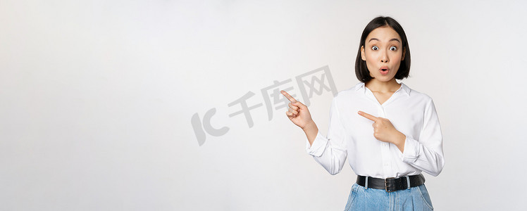 新店开业打折摄影照片_兴奋的年轻亚洲女性的肖像，办公室女士指着打折的手指，展示销售横幅，站在白色背景上