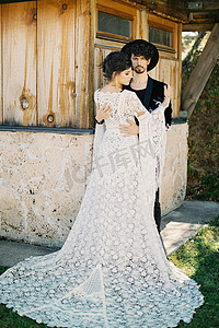 婚礼墙摄影照片_新郎在木屋墙边拥抱新娘