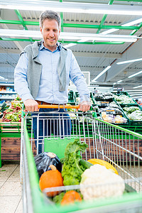 推南瓜摄影照片_男子在超市购物，推着蔬菜推车