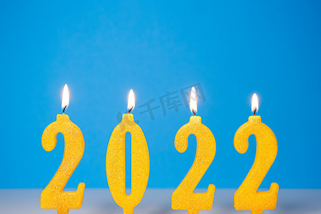 燃烧黄色蜡烛的假日背景2022年新年快乐概念燃烧黄色和金色2022蜡烛隔离在蓝色背景