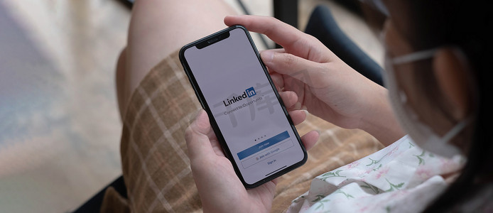 泰国清迈，2021 年 11 月 14 日：一位女士拿着苹果 iPhone X，屏幕上显示 LinkedIn 应用程序。LinkedIn 是一款智能手机照片共享应用程序。