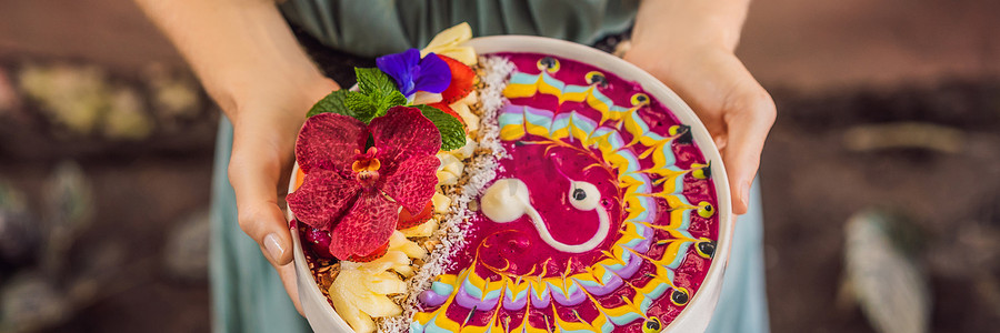 横幅，长格式 吃地中海早餐的年轻女子，吃健康的热带早餐，热带水果冰沙碗，装饰着彩色酸奶图案，配有姜黄和螺旋藻。