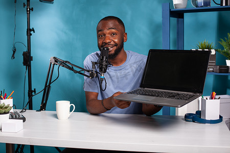 微笑的数字技术评论员手持带有黑屏模型录制播客的笔记本电脑