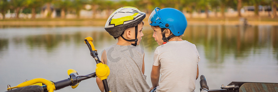 两个男孩骑自行车和踏板车后坐在湖岸上横幅，长格式