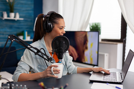女视频博主拿着杯子，使用笔记本电脑播放播客。