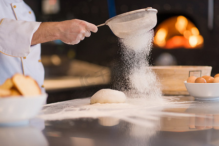 撒面粉摄影照片_厨师在新鲜的披萨面团上撒上面粉