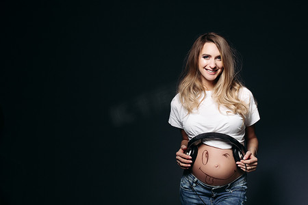 微笑的怀孕女性肚子上戴着大耳机。