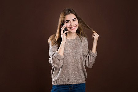 毛衣背景摄影照片_一个穿着毛衣的可爱快乐女孩在手机上聊天，在毛衣背景下大笑的肖像。