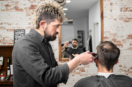 剪头发摄影照片_男理发师在理发店用剪刀给男性顾客剪头发。