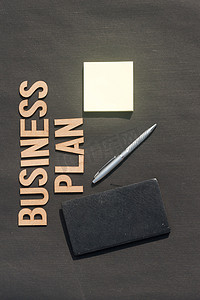 商人手把笔和笔记本放在由字母木块制成的Word商业计划前面。