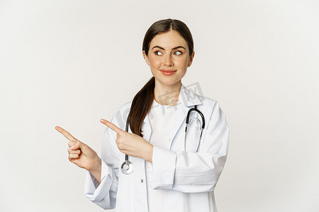微笑的年轻女医生、医疗保健医务人员的肖像，手指向左，展示诊所促销、标志或横幅，站在白色背景上