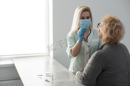 鼻拭子摄影照片_身穿个人防护装备的专业医务人员使用测试棒测试老年妇女是否患有危险疾病。