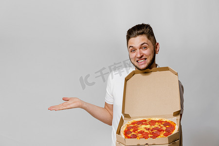 英俊的年轻快递员拿着披萨指向空的空间进行文字广告。